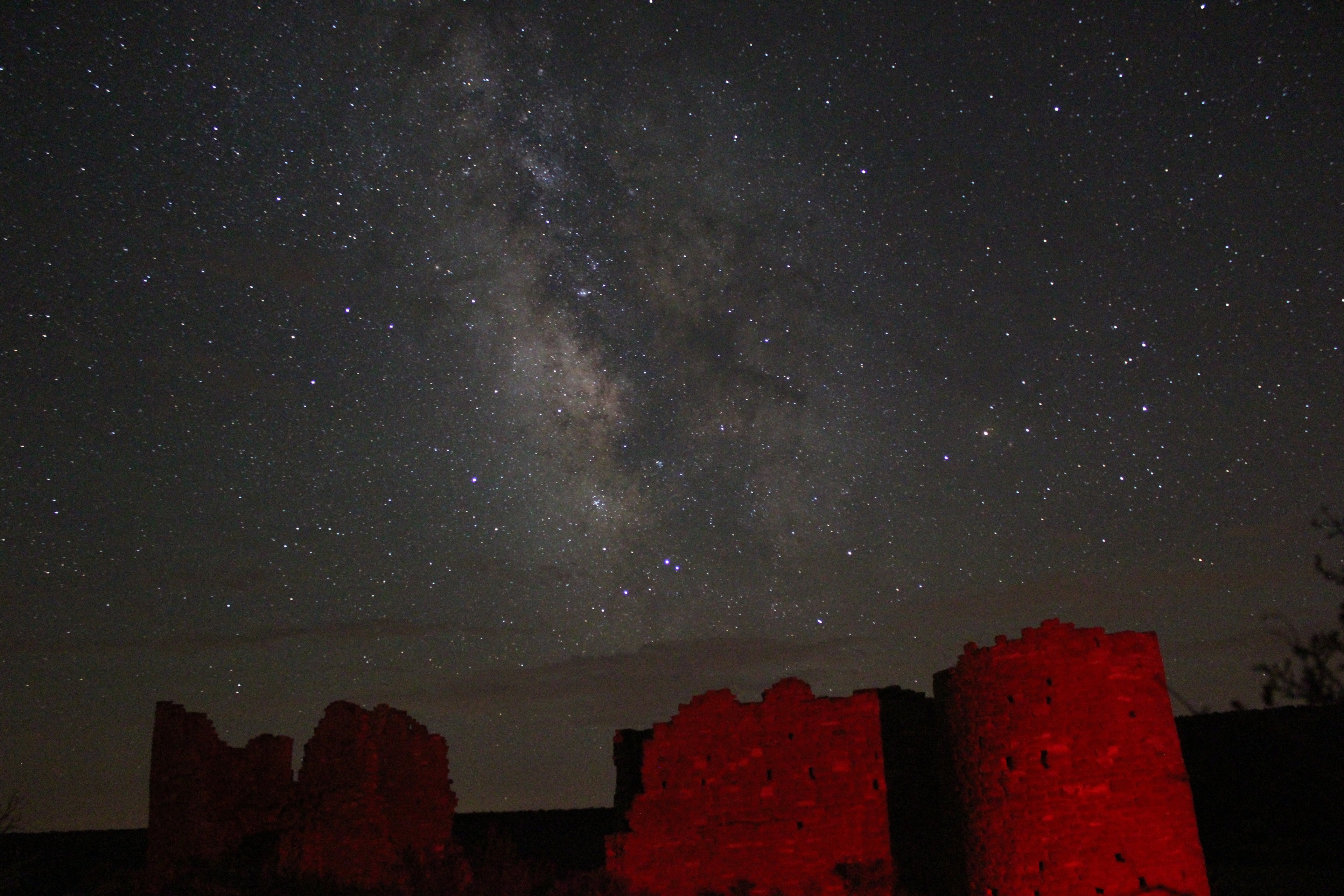 Ancient ruins lit red beneath the Milky Way near Bluff, Utah